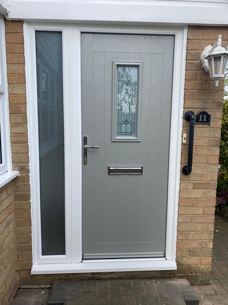 Grey front door with a glazed side panel on a brick house