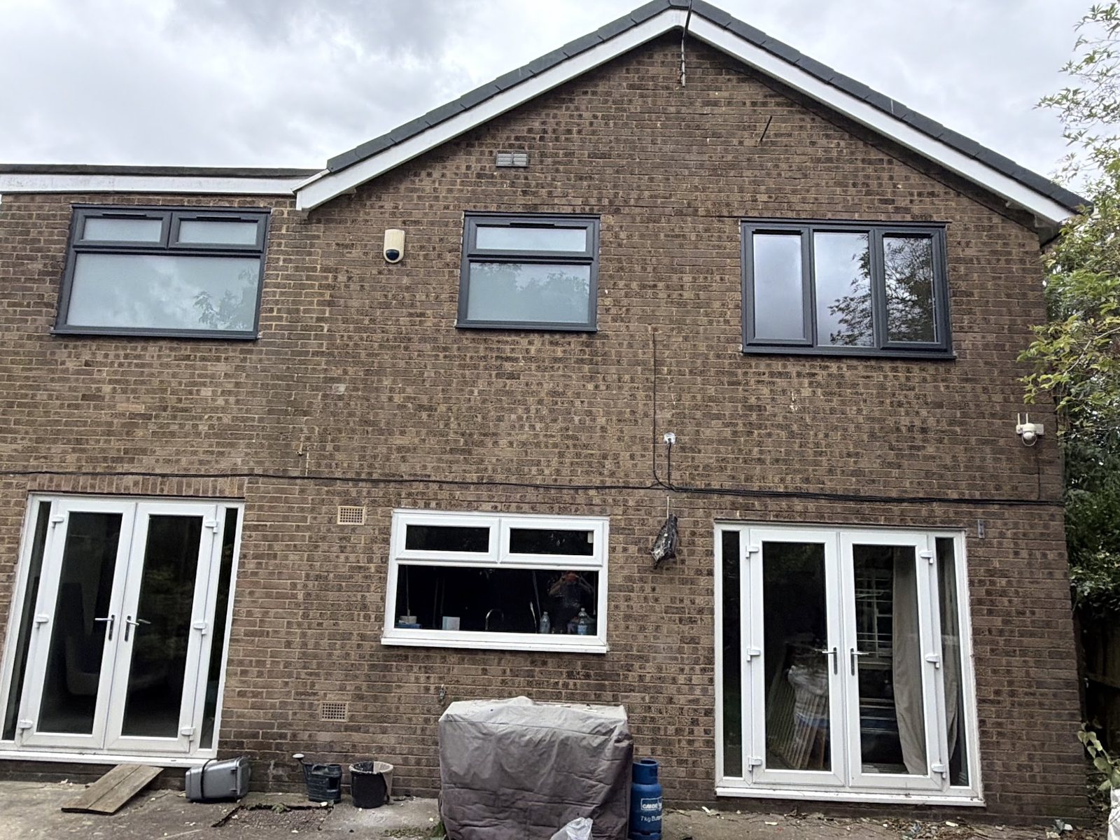 Back of a brick house with new grey windows upstairs and two sets of white french doors